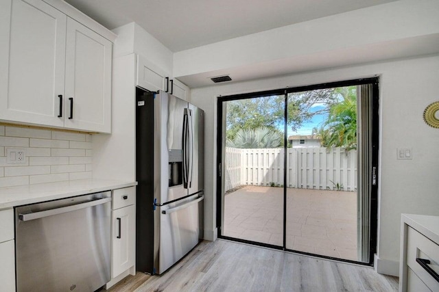 kitchen with white cabinets, appliances with stainless steel finishes, light wood-type flooring, and tasteful backsplash