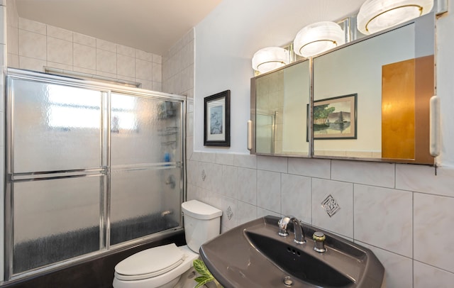 full bathroom with combined bath / shower with glass door, sink, decorative backsplash, toilet, and tile walls