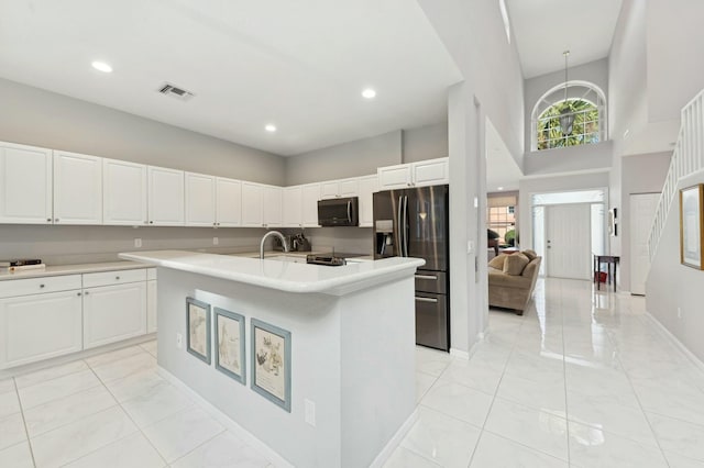 kitchen featuring a high ceiling, a center island with sink, white cabinets, sink, and stainless steel refrigerator with ice dispenser