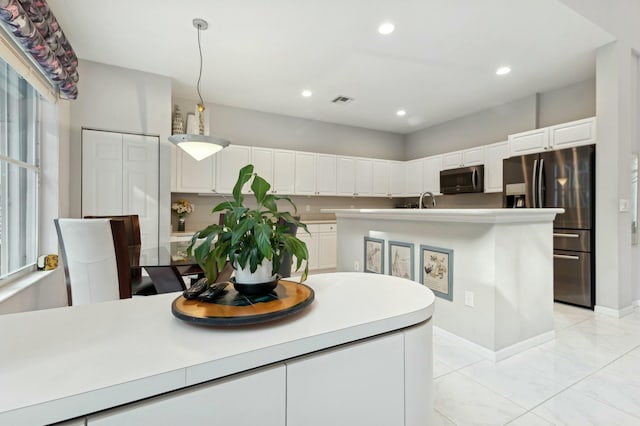 kitchen with stainless steel fridge, white cabinets, an island with sink, and decorative light fixtures