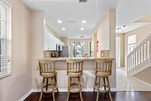 kitchen with white cabinetry, stainless steel appliances, a kitchen breakfast bar, kitchen peninsula, and decorative backsplash