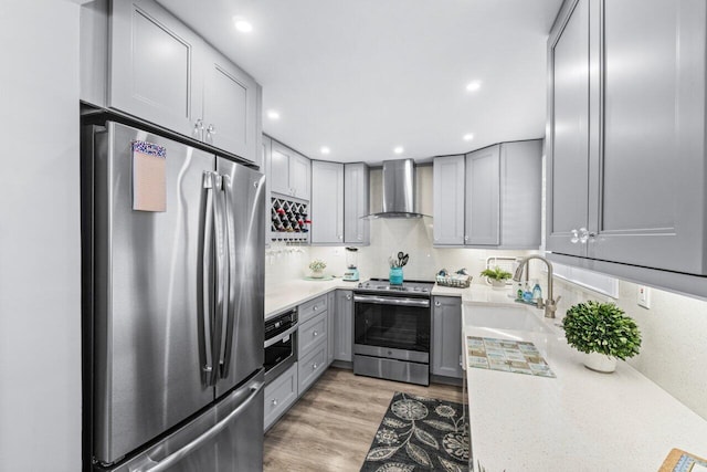 kitchen featuring wall chimney exhaust hood, gray cabinets, appliances with stainless steel finishes, and light countertops