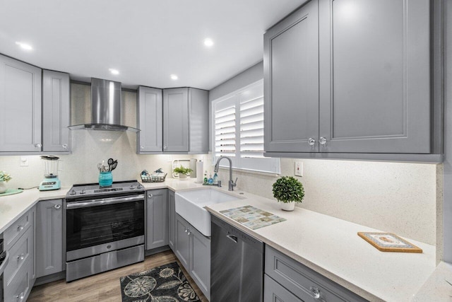 kitchen featuring wall chimney exhaust hood, stainless steel appliances, light countertops, gray cabinetry, and a sink