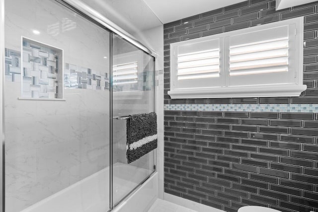 bathroom with toilet and shower / bath combination with glass door