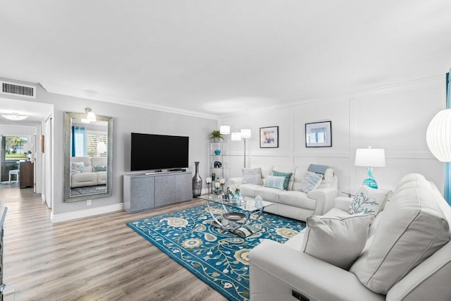 living area with baseboards, visible vents, wood finished floors, and ornamental molding