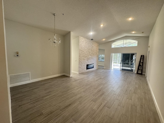 unfurnished living room featuring a textured ceiling, high vaulted ceiling, a stone fireplace, and a notable chandelier