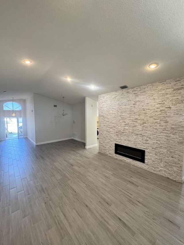 unfurnished living room featuring a textured ceiling, vaulted ceiling, wood-type flooring, a notable chandelier, and a stone fireplace