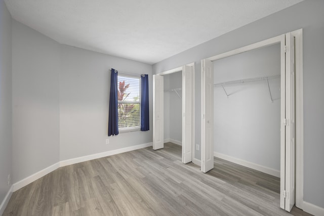 unfurnished bedroom with baseboards, a textured ceiling, wood finished floors, and multiple closets