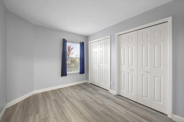 unfurnished bedroom with baseboards, wood finished floors, and multiple closets