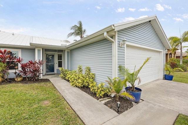 single story home featuring a front yard, metal roof, driveway, and an attached garage