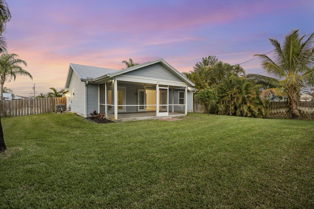 rear view of house featuring a lawn, central AC unit, a sunroom, metal roof, and a fenced backyard