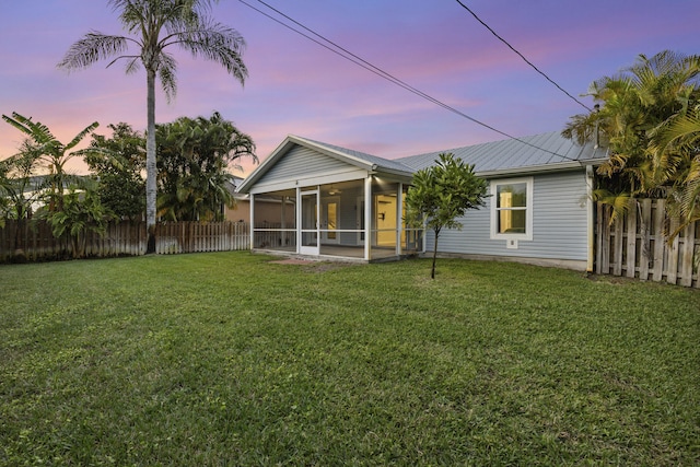 back house at dusk featuring a sunroom and a yard