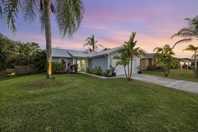 view of front of property featuring metal roof, a garage, fence, driveway, and a front yard