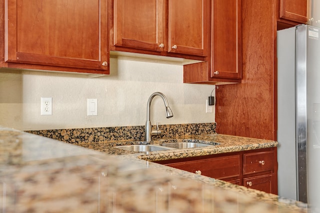 kitchen featuring stainless steel refrigerator, light stone countertops, and sink