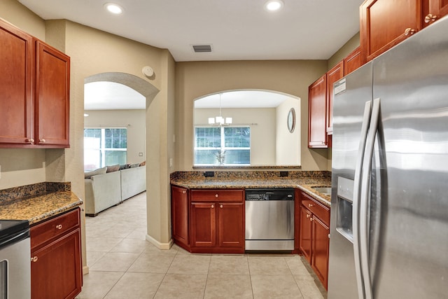 kitchen featuring pendant lighting, an inviting chandelier, dark stone countertops, light tile patterned floors, and stainless steel appliances