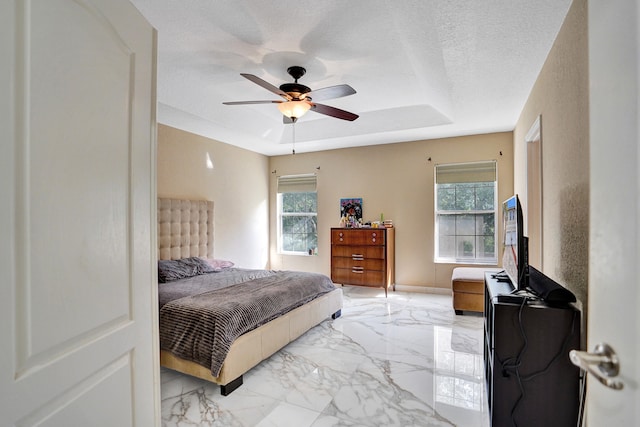 bedroom featuring a tray ceiling, ceiling fan, and a textured ceiling