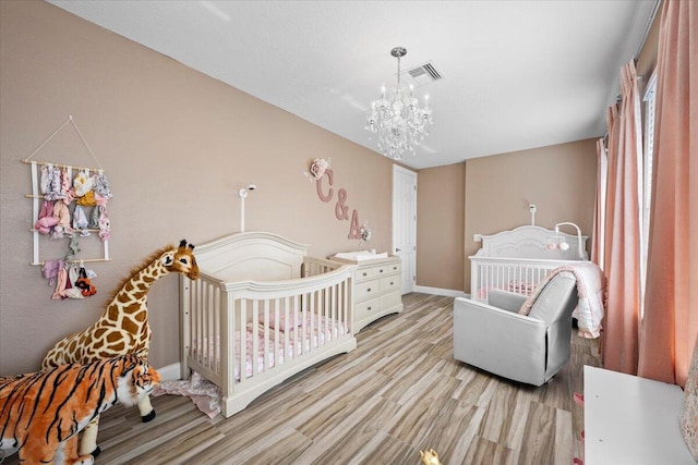 bedroom with light hardwood / wood-style flooring, a nursery area, and an inviting chandelier