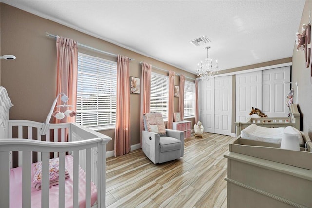 bedroom featuring a chandelier, light wood-type flooring, a closet, and a nursery area