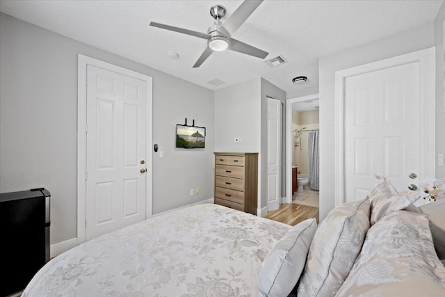 bedroom featuring ceiling fan, light wood-type flooring, a textured ceiling, and connected bathroom