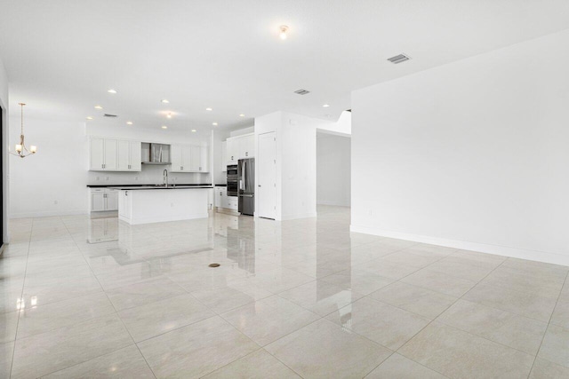 kitchen with stainless steel fridge, sink, wall chimney range hood, a center island with sink, and white cabinets