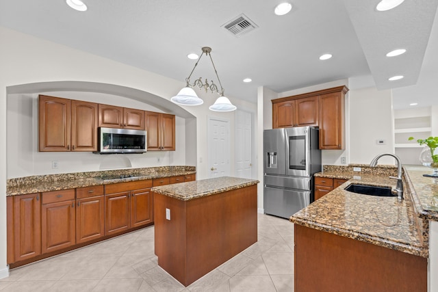 kitchen featuring sink, stone counters, appliances with stainless steel finishes, a center island, and decorative light fixtures