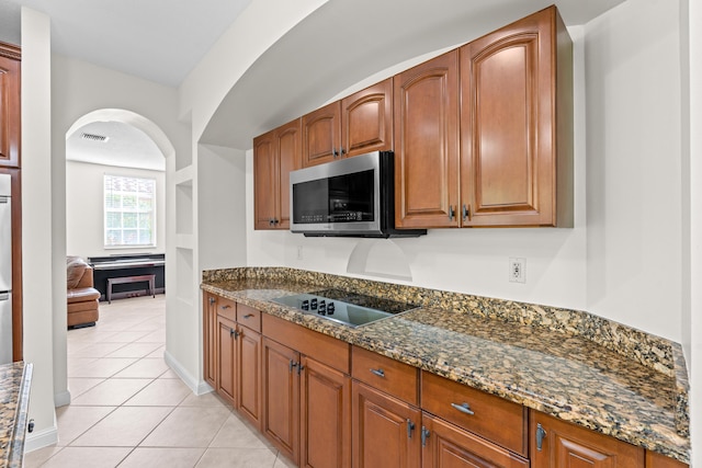 kitchen with black electric cooktop, light tile patterned flooring, and dark stone countertops