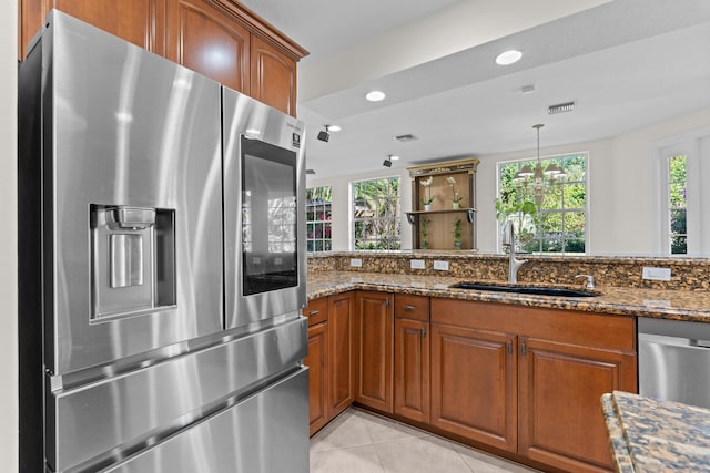 kitchen featuring sink, dark stone countertops, hanging light fixtures, stainless steel appliances, and light tile patterned flooring