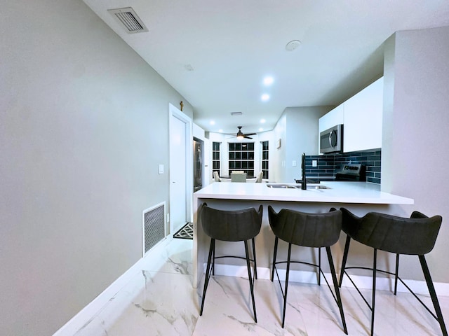 kitchen featuring white cabinetry, sink, backsplash, kitchen peninsula, and a breakfast bar