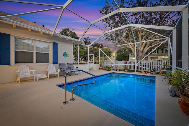 pool at dusk with glass enclosure and a patio