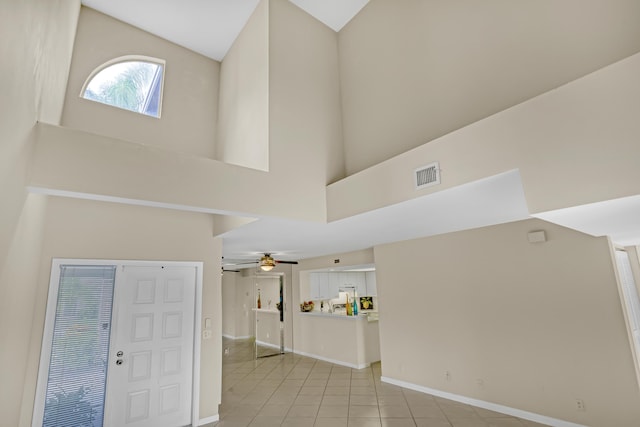 foyer with ceiling fan, a towering ceiling, and light tile patterned flooring