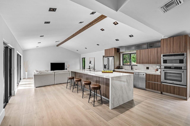 kitchen featuring stainless steel appliances, a spacious island, light hardwood / wood-style floors, decorative backsplash, and a kitchen breakfast bar