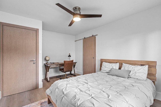 bedroom featuring a barn door, wood finished floors, and a ceiling fan