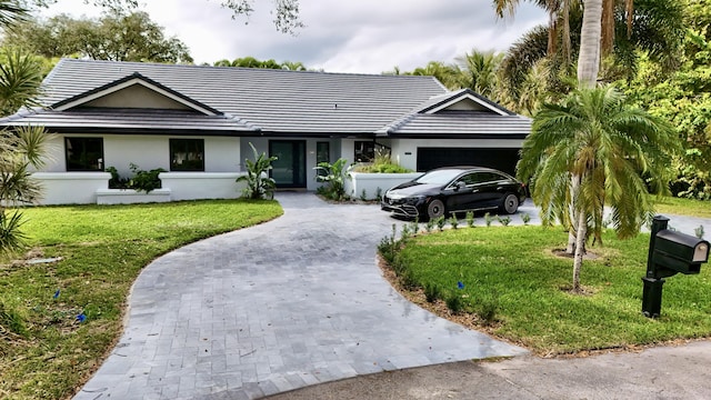 ranch-style home featuring a garage, a tiled roof, decorative driveway, a front yard, and stucco siding