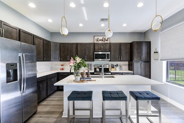 kitchen featuring appliances with stainless steel finishes, a center island with sink, dark brown cabinets, and pendant lighting