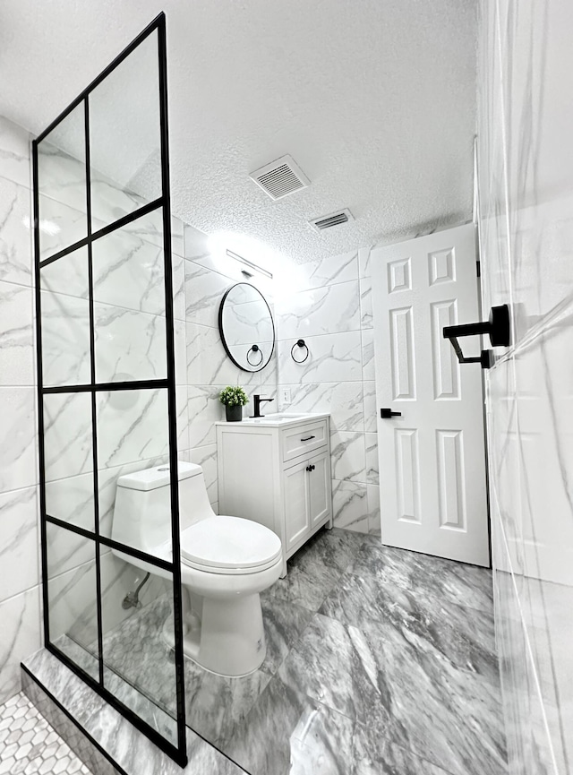 bathroom with vanity, toilet, a textured ceiling, tile walls, and a tile shower