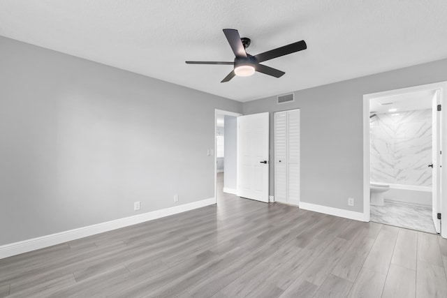 unfurnished bedroom with ensuite bathroom, ceiling fan, a textured ceiling, light hardwood / wood-style floors, and a closet