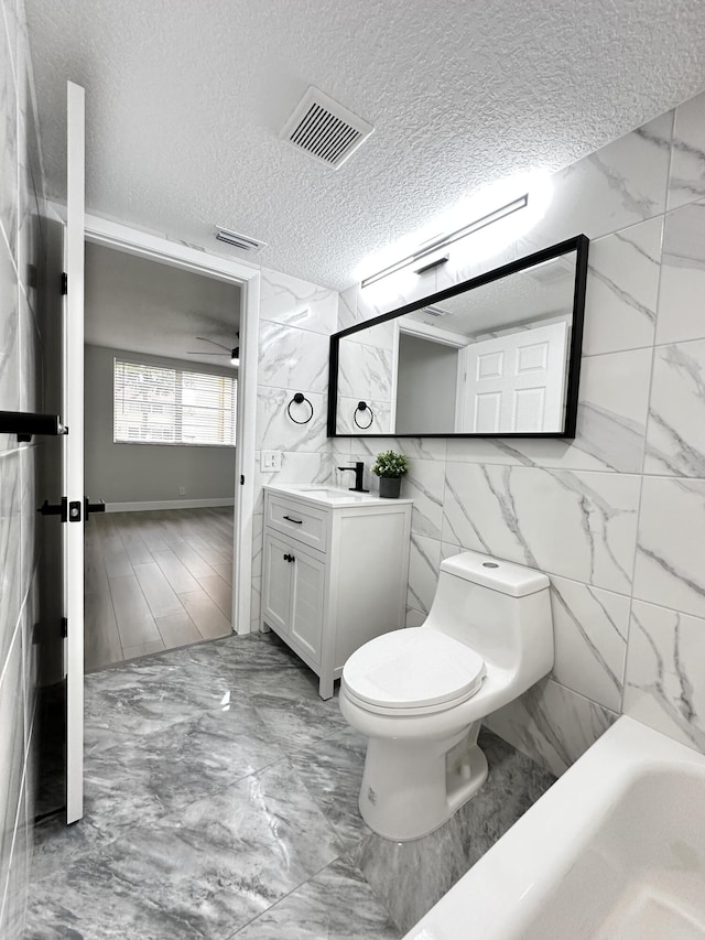 full bathroom featuring vanity, a textured ceiling,  shower combination, tile walls, and toilet