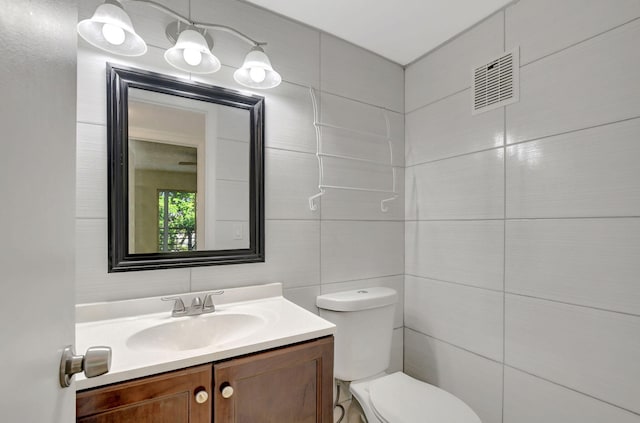 bathroom featuring vanity, toilet, and tile walls