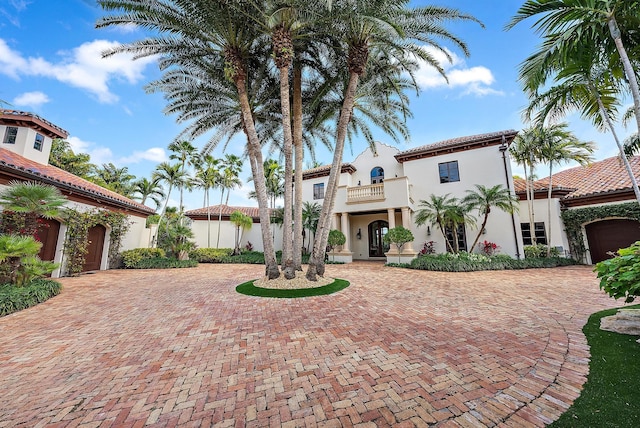 view of front of house with a tiled roof, stucco siding, decorative driveway, a garage, and a balcony