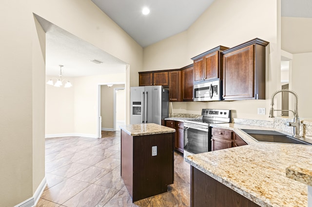 kitchen with sink, a kitchen island, light stone counters, stainless steel appliances, and a chandelier