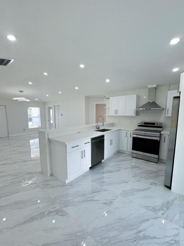 kitchen with kitchen peninsula, appliances with stainless steel finishes, sink, wall chimney range hood, and white cabinets