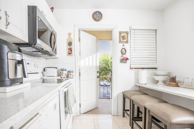 kitchen featuring white cabinets, light stone counters, white appliances, a breakfast bar, and light tile patterned floors