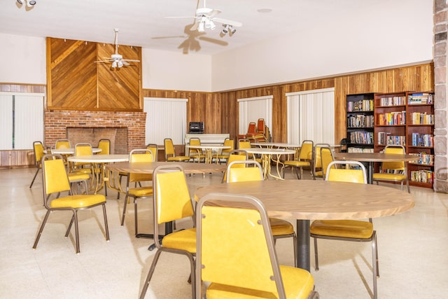 dining room featuring wood walls, a fireplace, a towering ceiling, and ceiling fan