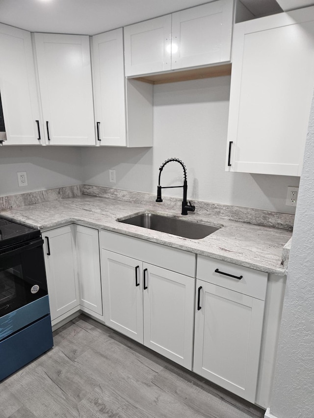 kitchen featuring light stone countertops, sink, white cabinets, light hardwood / wood-style floors, and black range with electric stovetop