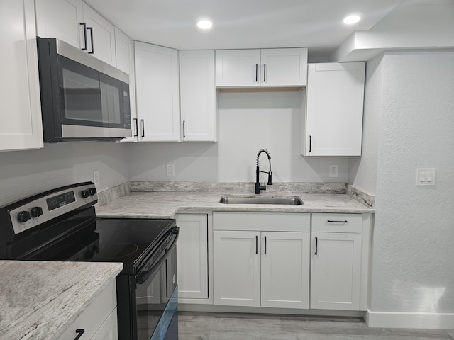 kitchen featuring white cabinets, sink, light stone countertops, appliances with stainless steel finishes, and light hardwood / wood-style floors