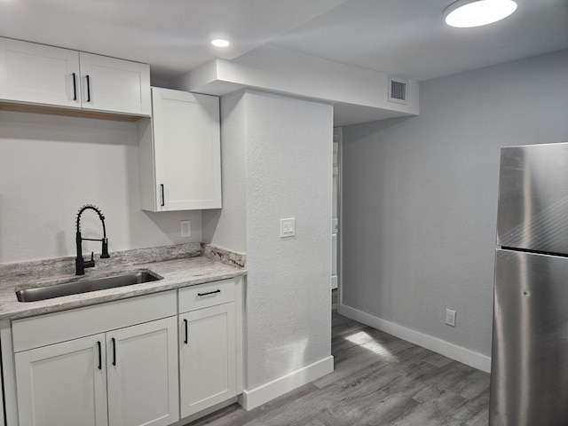 kitchen featuring white cabinets, sink, stainless steel fridge, light stone countertops, and light hardwood / wood-style floors