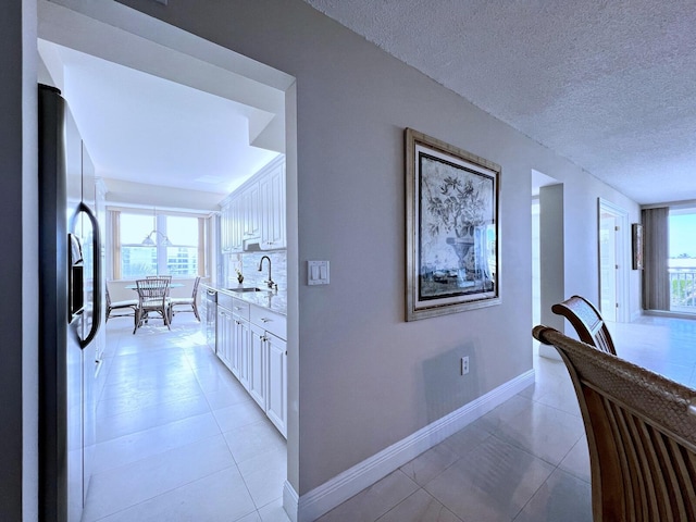 corridor featuring sink, light tile patterned floors, and a textured ceiling