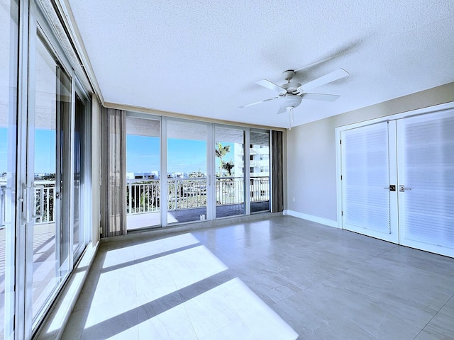 empty room with ceiling fan, a healthy amount of sunlight, a wall of windows, and a textured ceiling