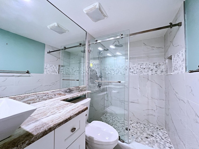 bathroom with a shower with door, vanity, tile walls, and toilet