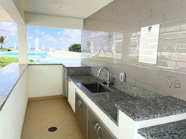 kitchen featuring tasteful backsplash, sink, light tile patterned floors, dark stone countertops, and white cabinets